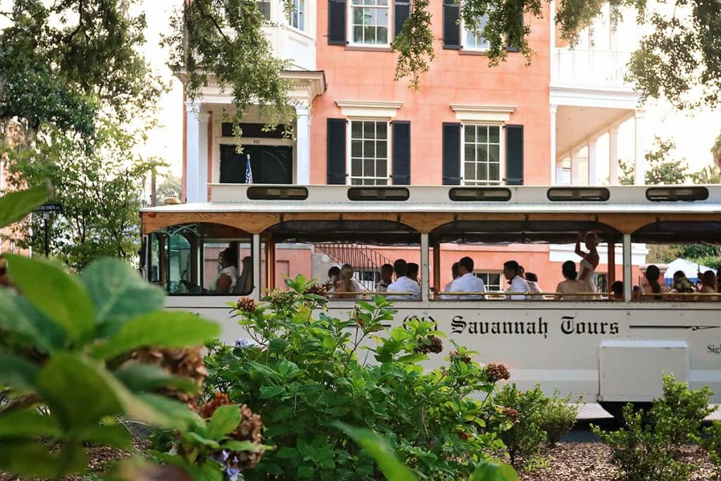 A white Old Savannah Tours trolley passes in front of a salmon-colored mansion at 432 Abercorn Street in Savannah