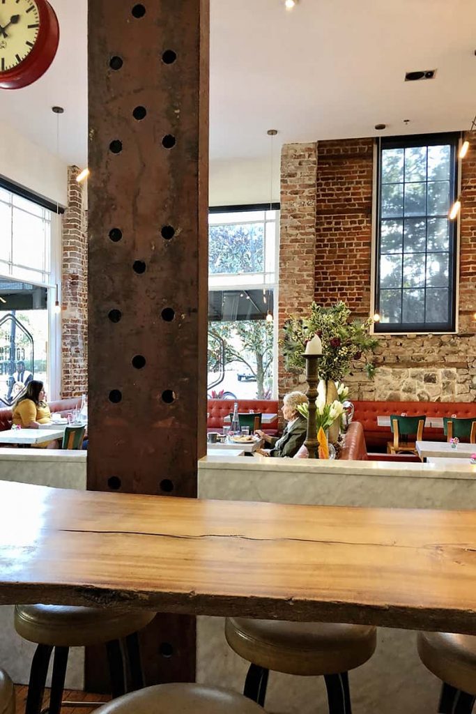 Interior of The Collins Quarter restaurant in Savannah with exposed brick walls, red leather seating, and a raw-edged wood bartop