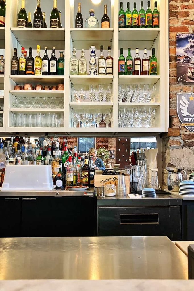 White shelves full of bar supplies with a girl reflected i the mirror at The Collins Quarter in Savannah