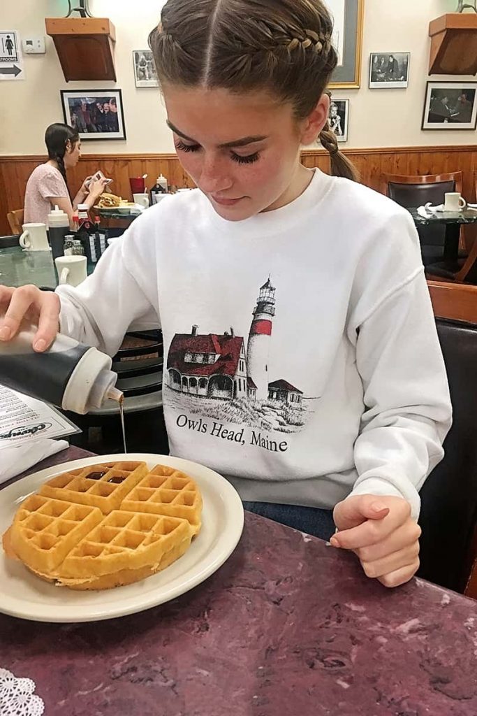 A young girl with braided pigtails pours syrup over a waffle in Clary's Cafe Savannah