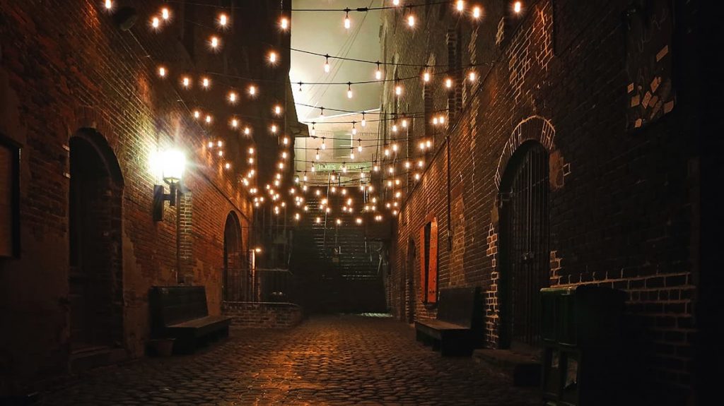 A dark riverfront alleyway along River Street dimly lit by twinkle lights and leading to a treacherous stone staircase