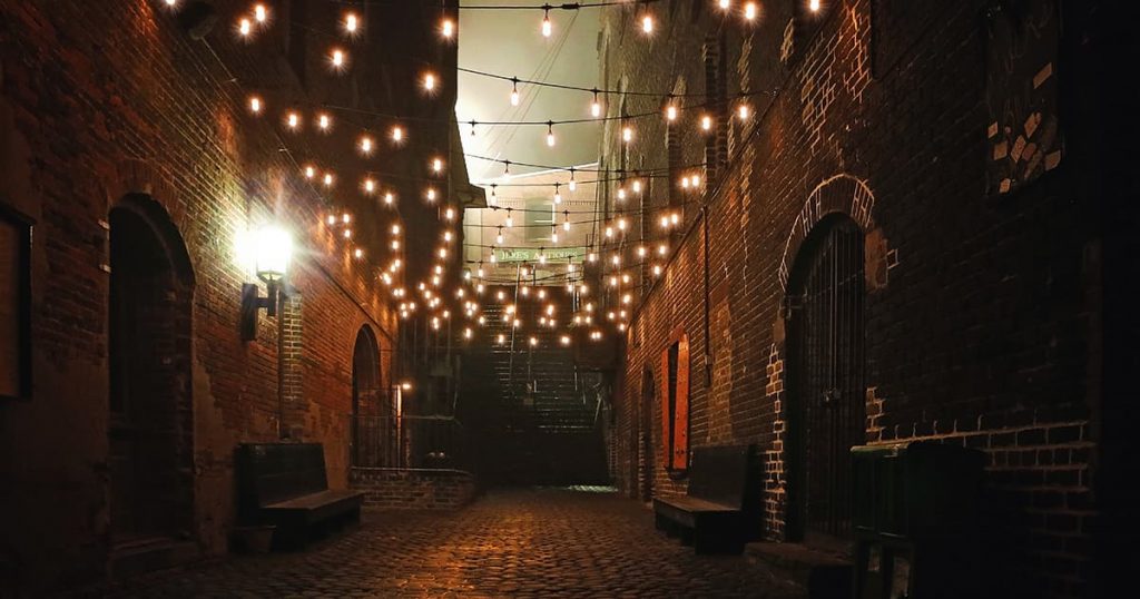 A dark riverfront alleyway dimly lit by twinkle lights leading to haunted Savannah's treacherous Stone Stairs of Death