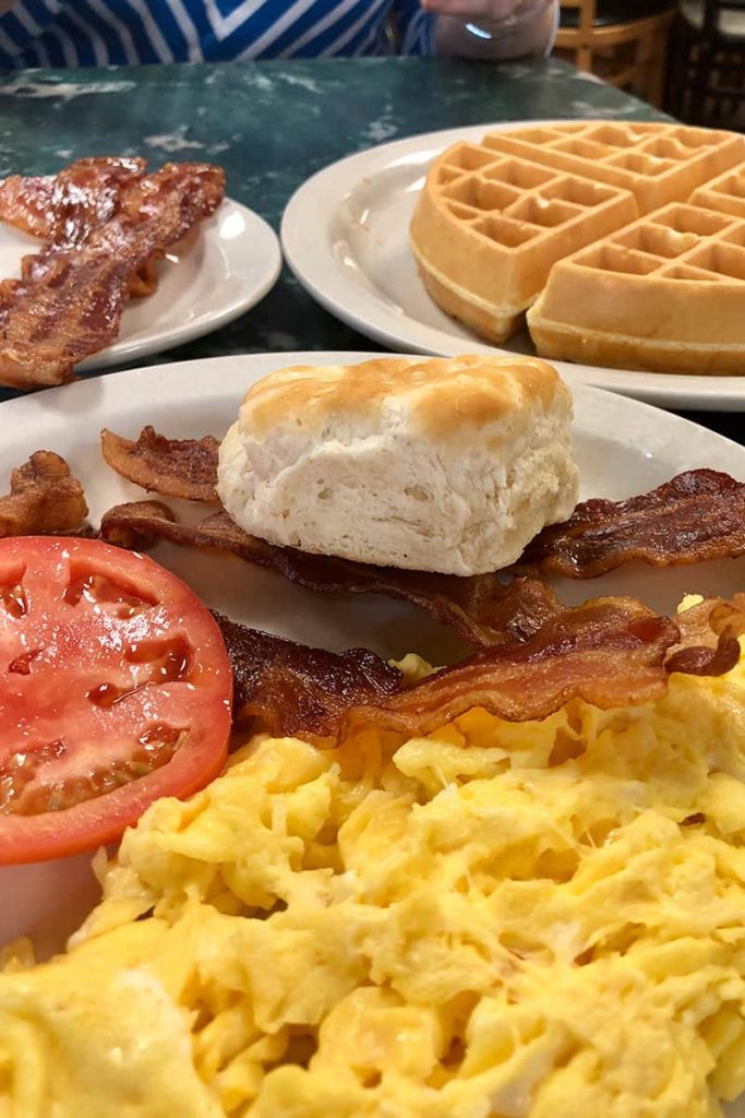 A breakfast plate at Savannah's Clary's Cafe showing hearty portions of scrambled eggs, crispy bacon, waffles, a biscuit, and tomato