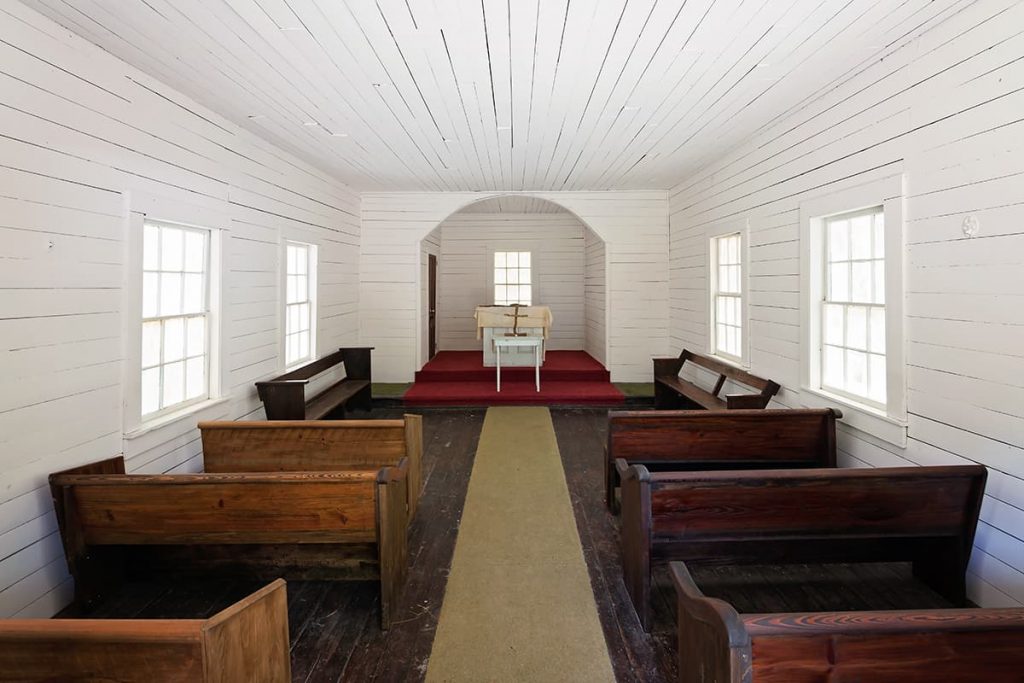 The humble interior of First African Baptist Church on Cumberland Island with shiplap walls and ceilings painted white, bare wood floors, and six old wooden pews