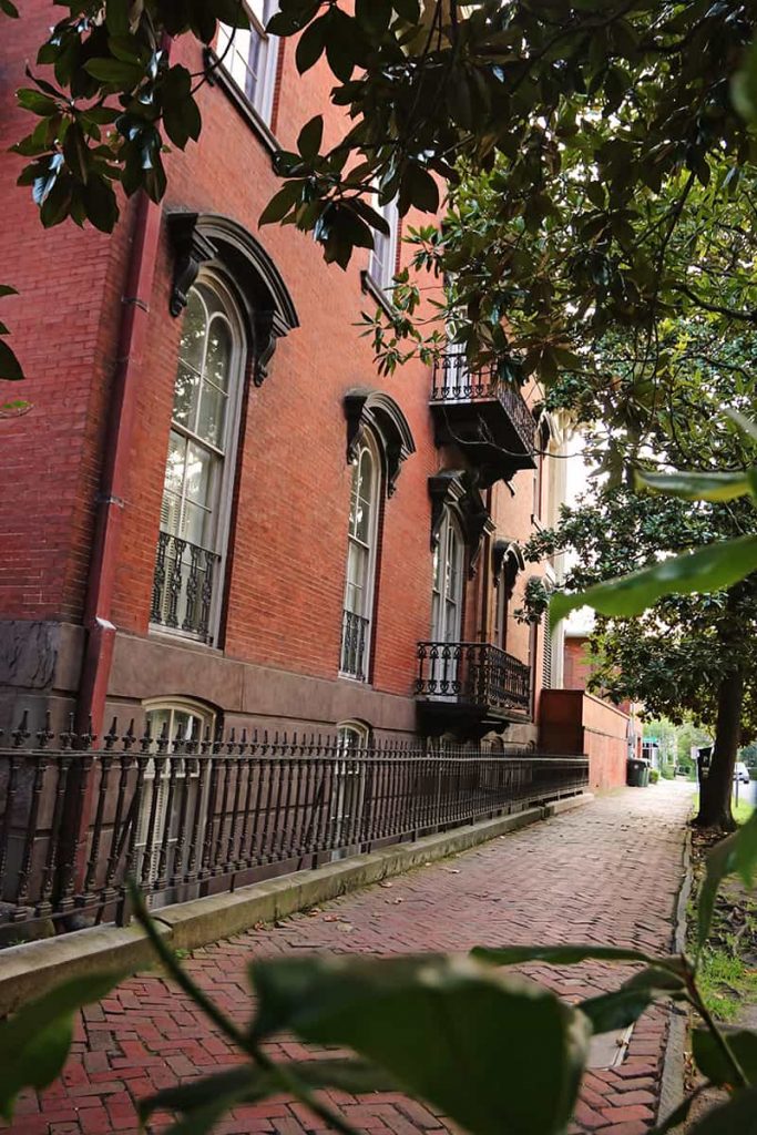 View of the north-facing side of Mercer Williams House with a historic brick sidewalk and spike-tipped wrought iron fence.