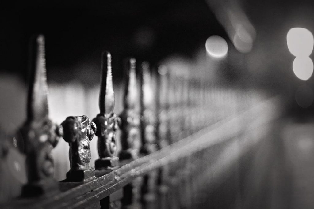 Moody B&W image of a black wrought-iron fence with one spike missing