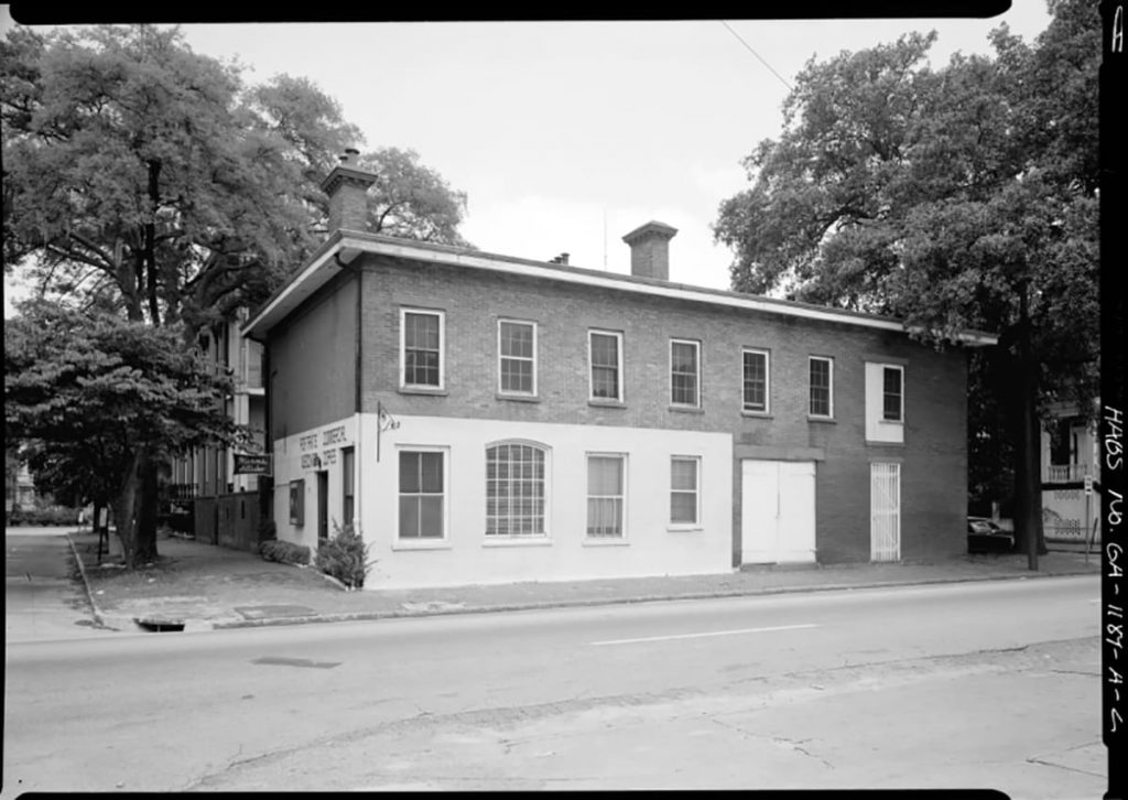 Historic B&W photo of the Mercer Williams carriage house with the bottom left portion of the house painted white and the remainder of the carriage house as unpainted bricks