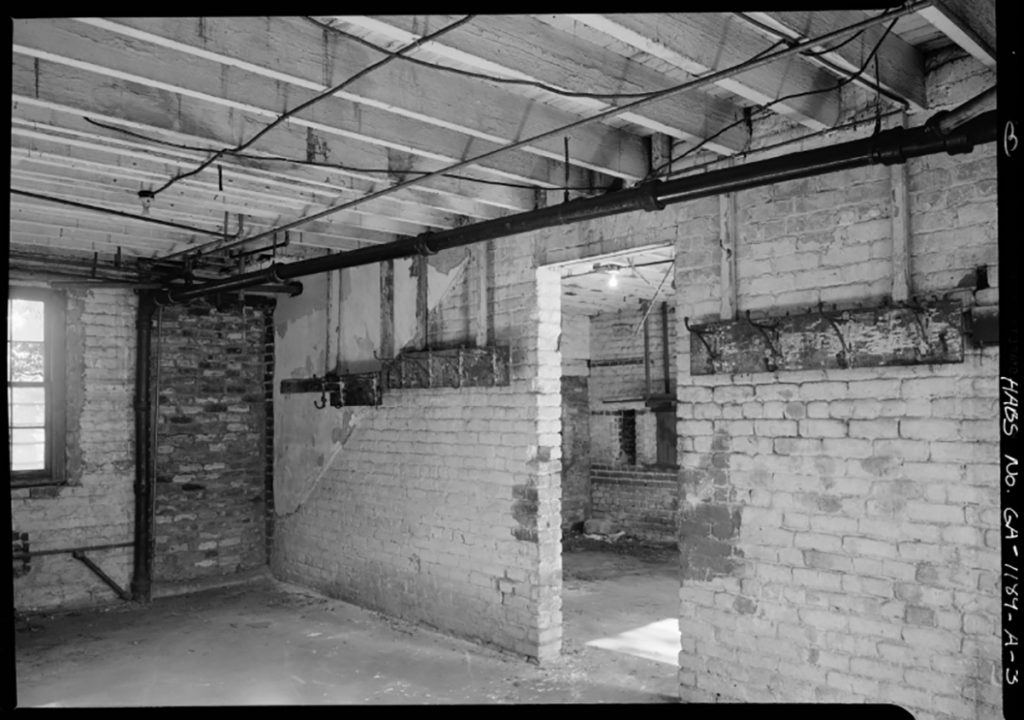 Interior of the Mercer Williams carriage house with exposed rafters in the ceiling, exposed brick walls painted white, and visible pipes along the ceiling