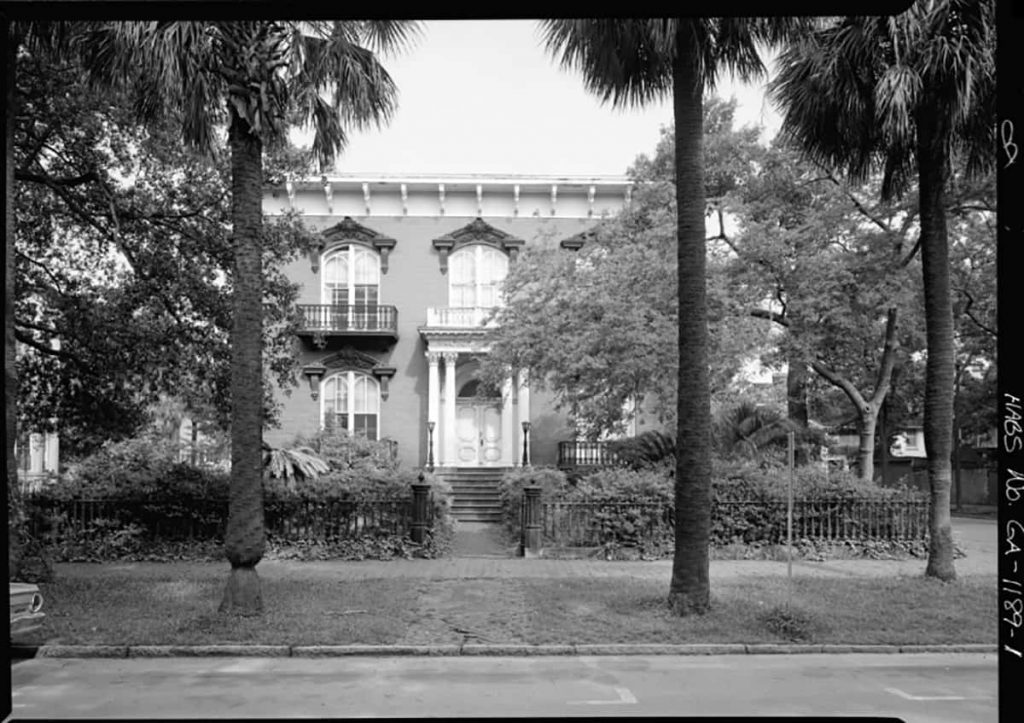 Historic B&W photo of the front façade of the Mercer Williams House with four palm trees visible in the tree lane