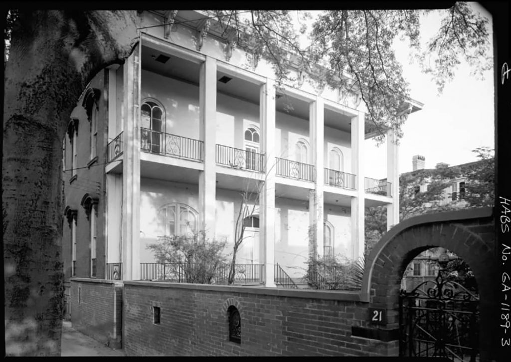 Two-story back porch with white columns and a low brick wall with windows and doors protected by iron scrollwork