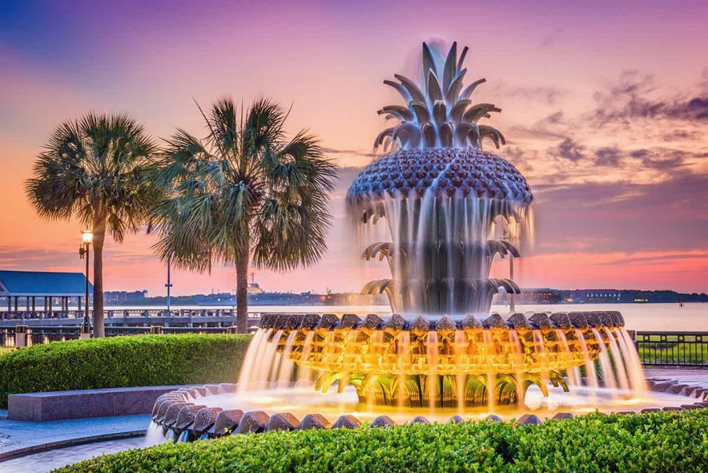 A typical Lowcountry South Carolina scene of the famous Charleston pineapple fountain with a pink and purple sunset in the background