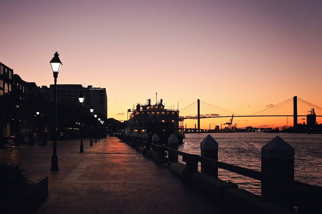 Riverfront plaza along River Street at dusk with the Savannah River and Talmadge bridge in the distance