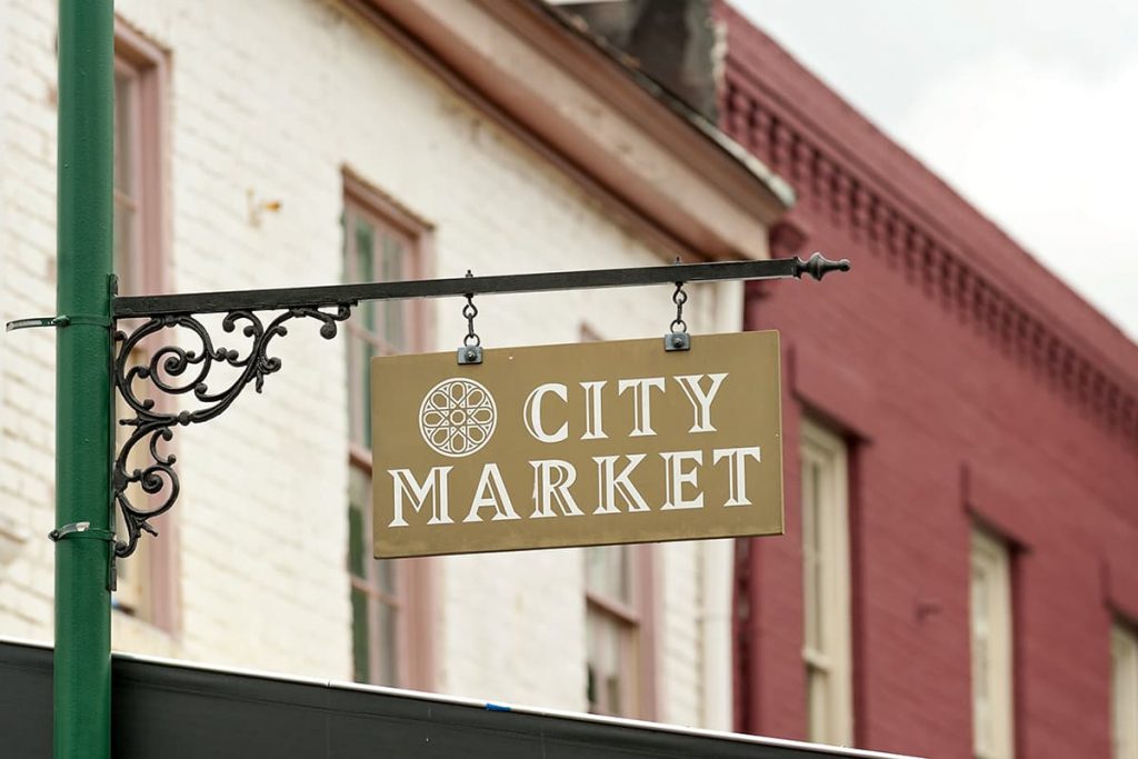 Gold sign with white lettering that reads City Market, and historic brick buildings in the background