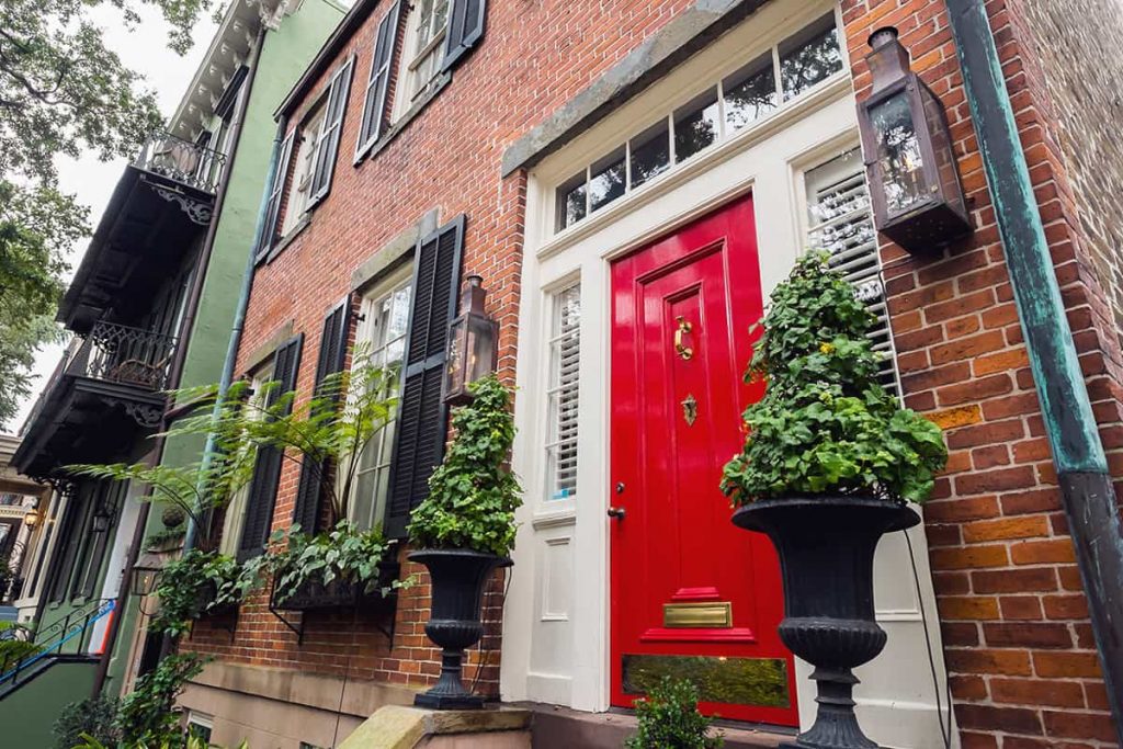 Facade of a historic brick home on Jones Street in Savannah with a bright red door and gas lanterns