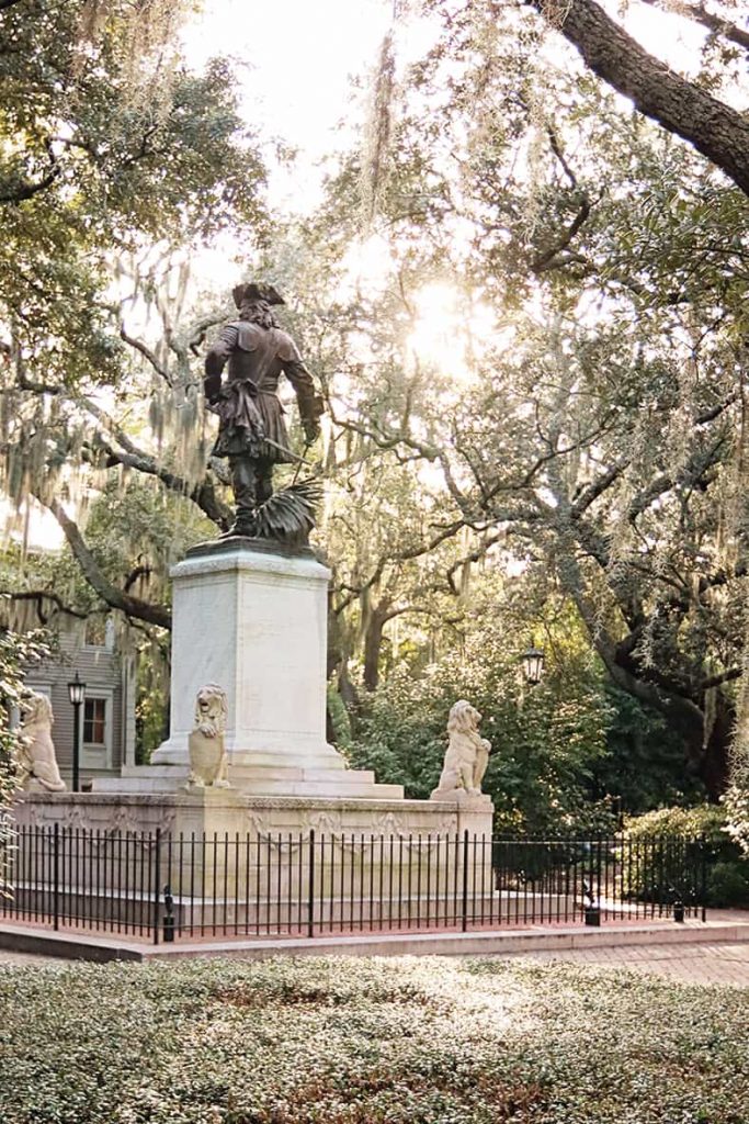 Sunlight streaming through the trees, highlighting a statue in Chippewa Square