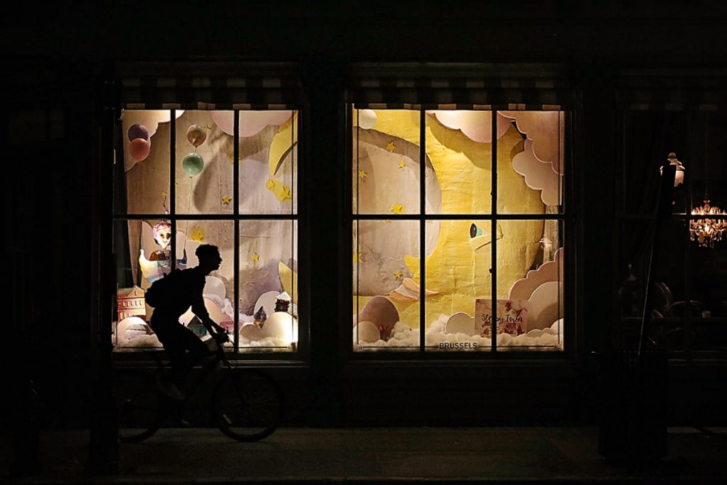A bicyclist silhouetted against a nighttime Christmas window display at The Paris Market in Savannah