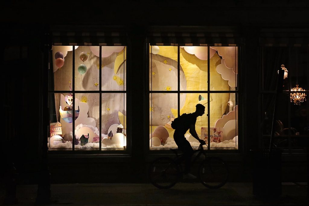 A bicyclist silhouetted against a nighttime Christmas window display at The Paris Market in Savannah