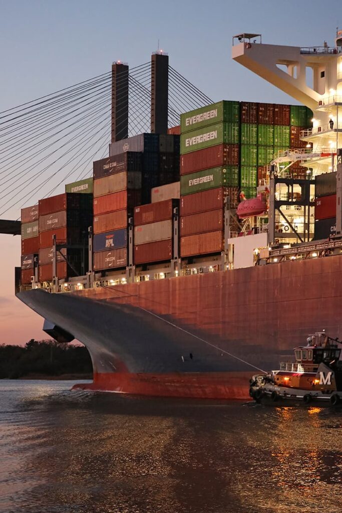 A massive cargo ships travels towards the Talmadge bridge at sunset along River Street -- a Savannah Georgia Must-See spot