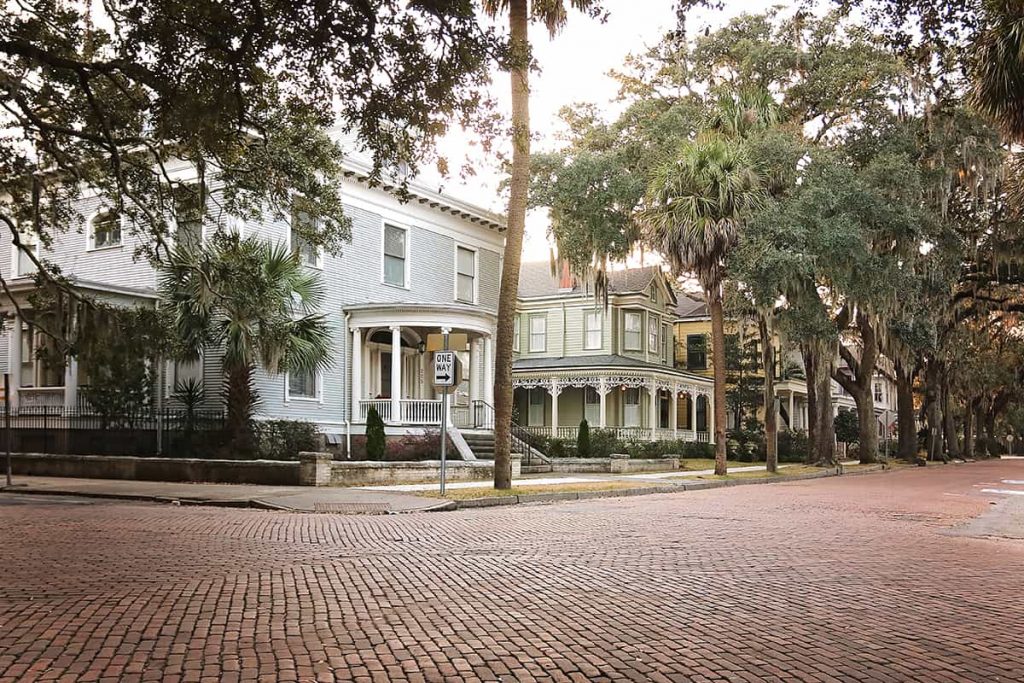 Intersection of two brick-paved streets lined with well-maintained Victorian homes and mature trees