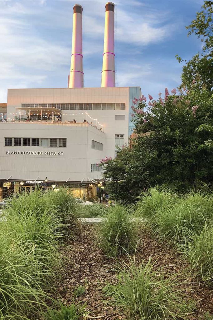 Plant Riverside District sign on the side of a white building that has a rooftop bar and two smokestacks on the roof