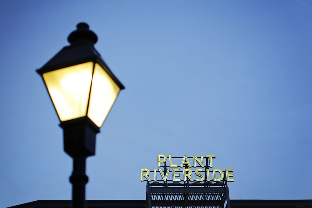 Old-timey lamppost in the foreground with a neon sign for Plant Riverside in the background