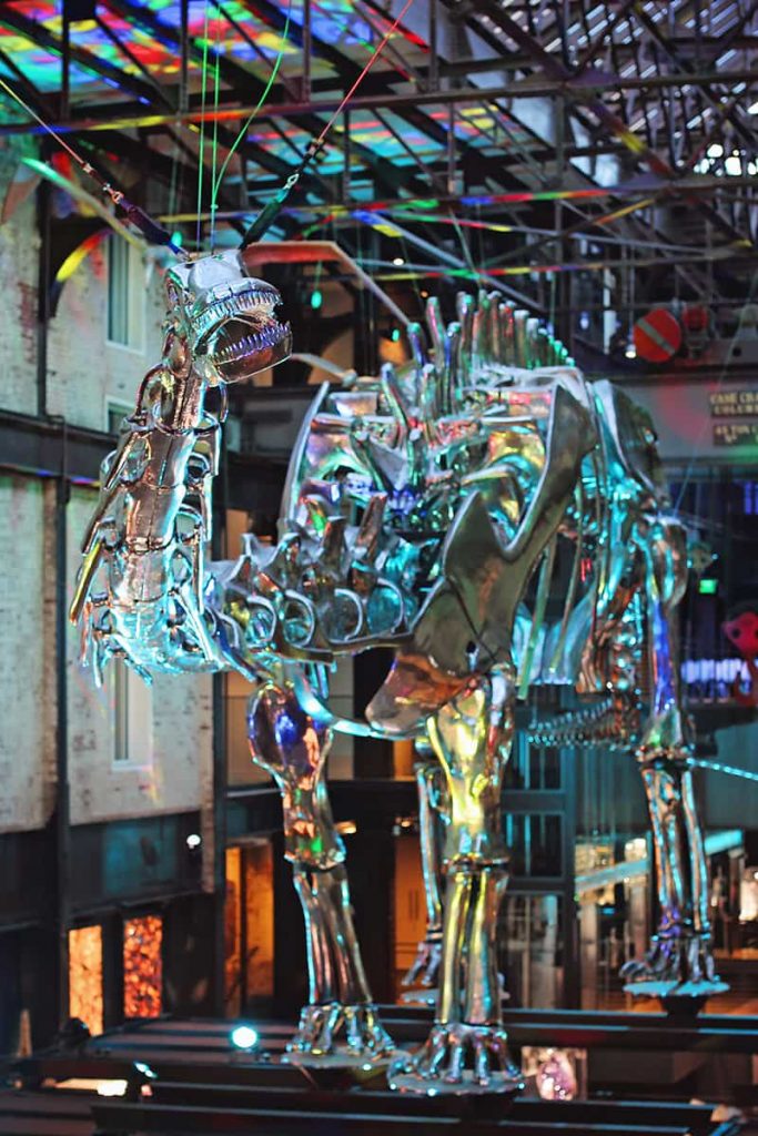 Front-facing shot of the Plant Riverside District's chrome dinosaur lit by rainbow-colored lighting