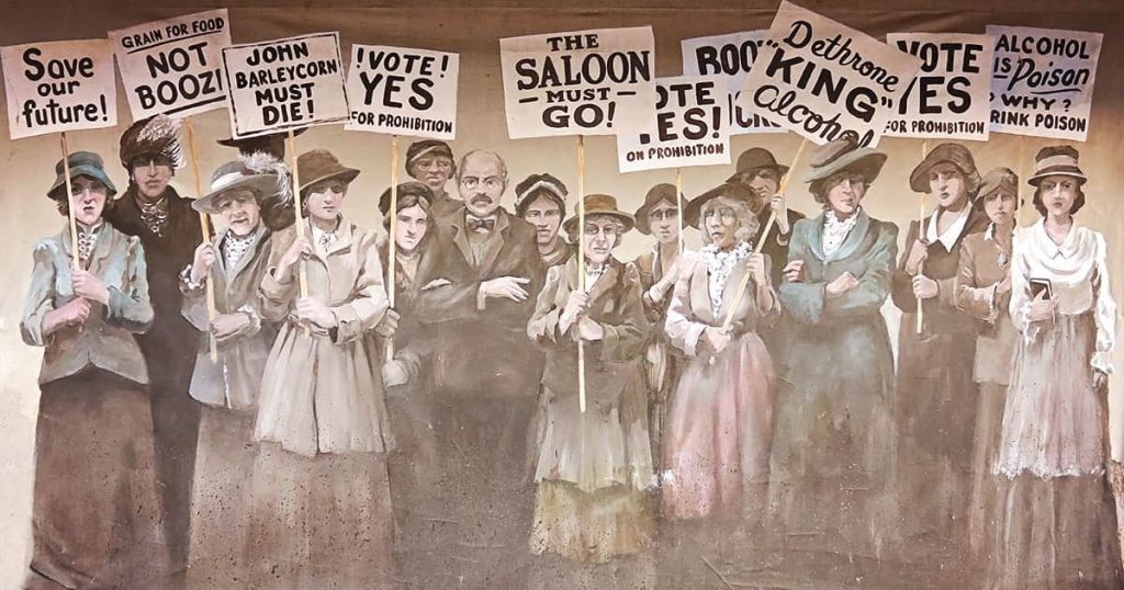 Hand-painted sign on a wall in City Market showing women dressed in period attire with signs advocating for Prohibition