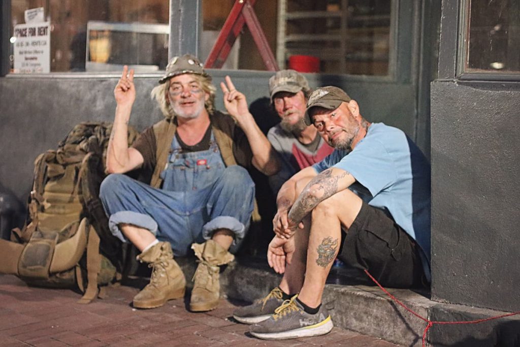 Three men pose for a photo while sitting in a doorway, one is displaying peace signs