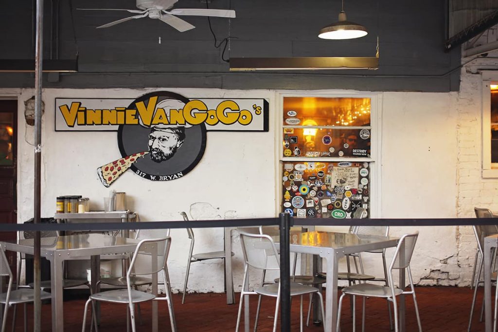 Metal tables at an outdoor cafe with a sign for Vinnie Van Go Go's in the background