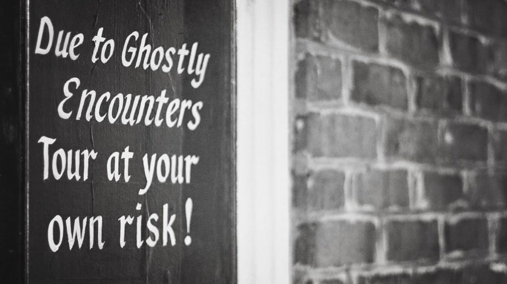 Hand-painted sign on a brick wall in Savannah that reads "Due to Ghostly Encounters - Tour at your own risk!"