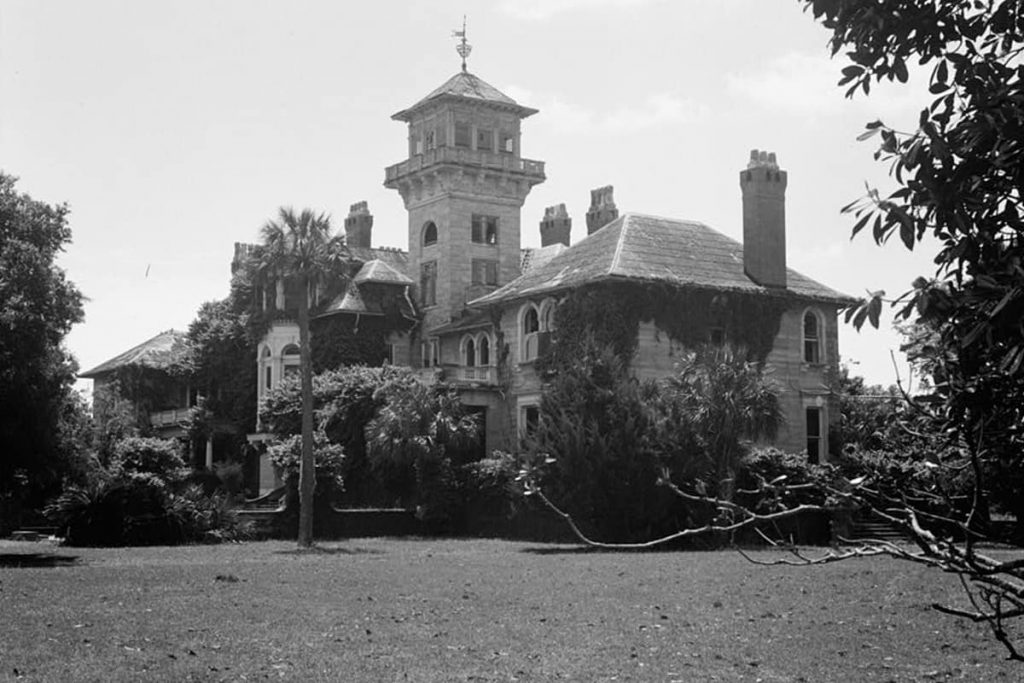 B&W image of a side view of the stately Dungeness Mansion with ivy climbing many of the exterior walls and what appears to be a turret at the center of the home