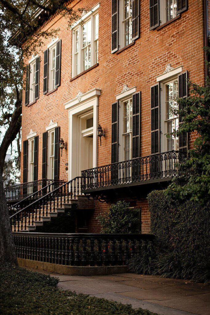 Stately brick mansion with wrought iron balconies and large windows framed by black shutters