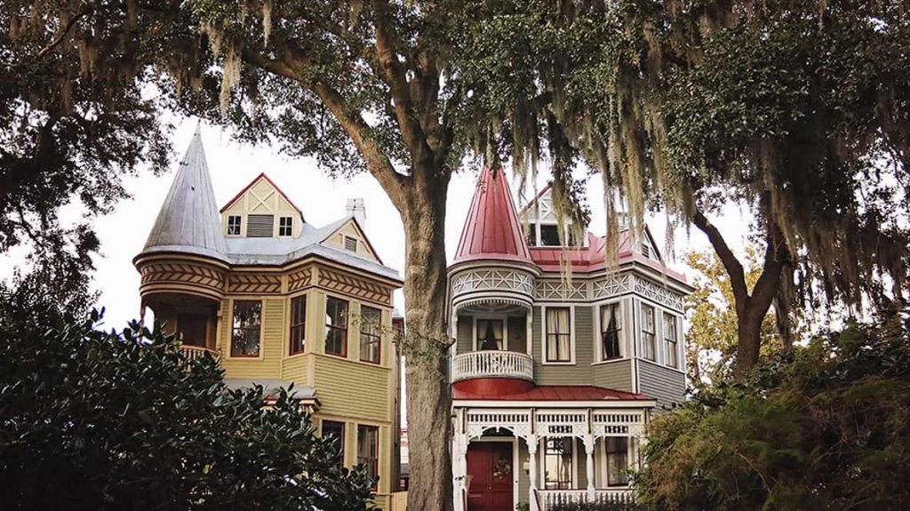 The "Victorian Twins" -- two identical and side-by-side Victorian-style houses in Savannah. One as a red roof and is painted in a sage green and white color scheme while the other has a tin roof and features a yellow and red paint scheme.
