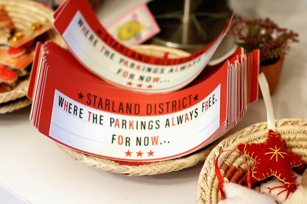 Red and white bumper stickers with black text that reads "Starland District: where the parking's always free...for now"