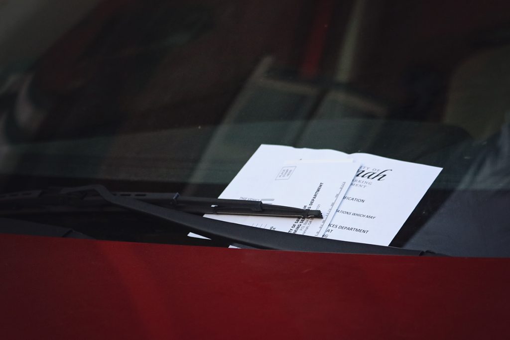 The hood of a burgundy-colored vehicle with a City of Savannah parking ticket tucked under black windshield wipers