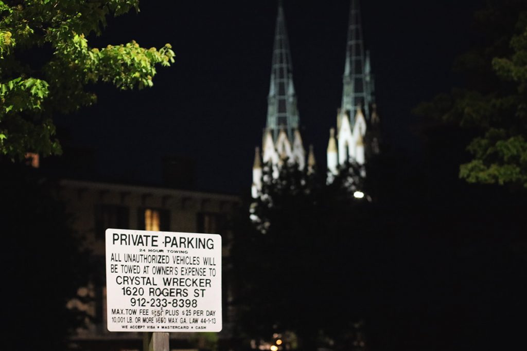 Nighttime scene with a Private Parking sign posted and two spires of the Cathedral Basilica of St. John the Baptist visible in the distance