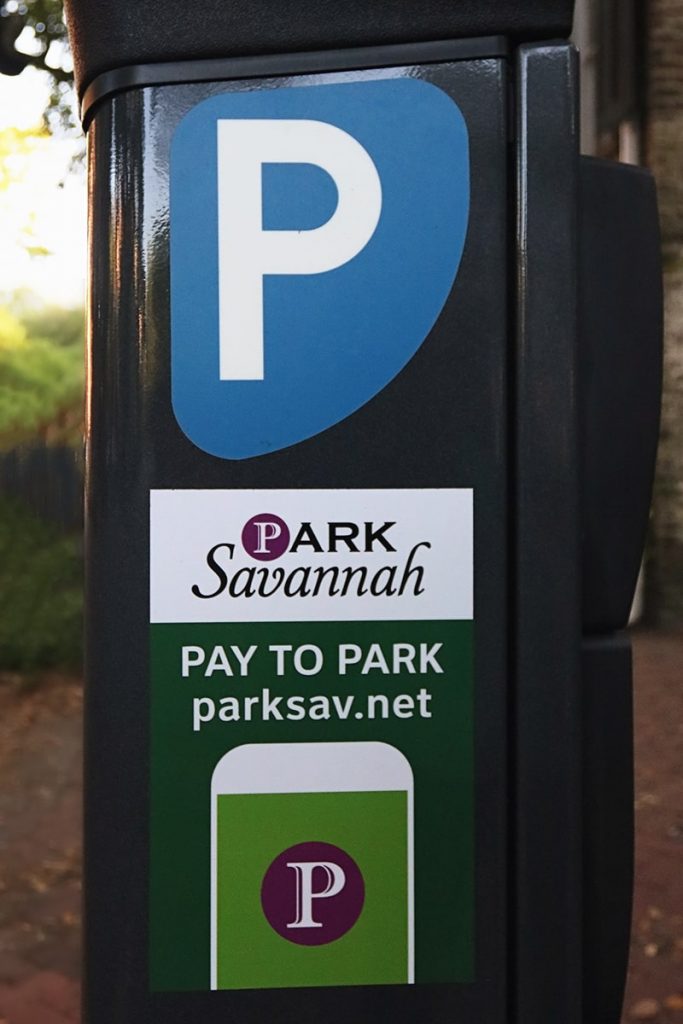 The side of a black metal parking kiosk with a green, white, and purple ParkSavannah logo and a blue parking in Savannah sticker