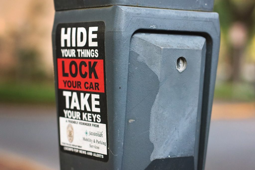 Sticker on the side of a parking meter in Savannah with a message from the Savannah Police Department saying Hide Your Things Lock Your Car Take Your Keys in bold black and white lettering on a red background