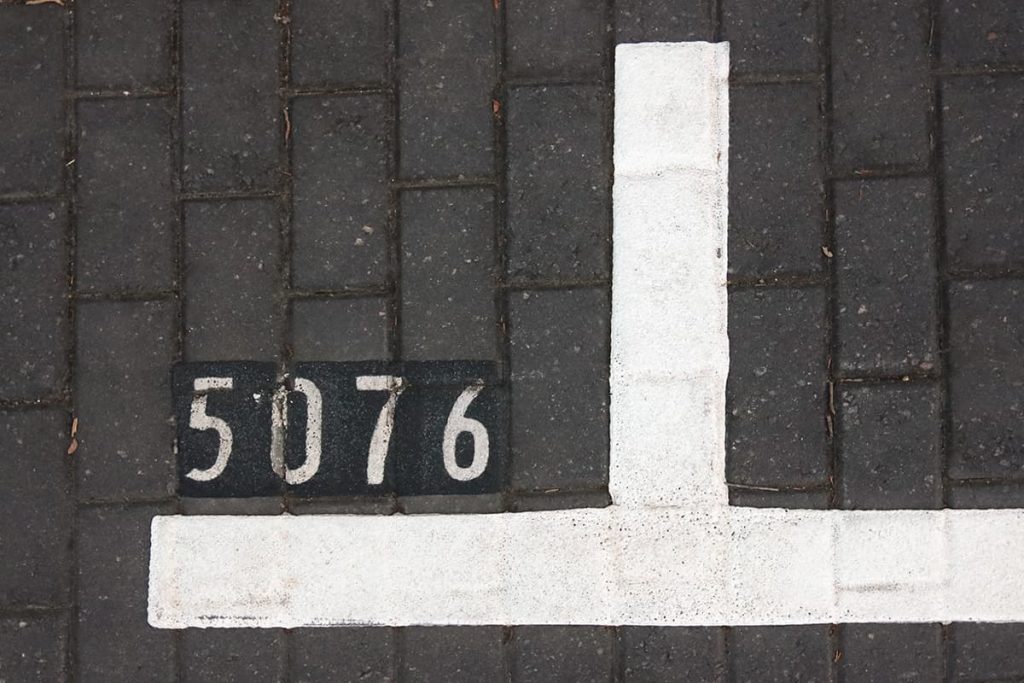 Road paved with grey Belgium blocks with parking lines painted in white and the numbers 5076 painted in white on a black background