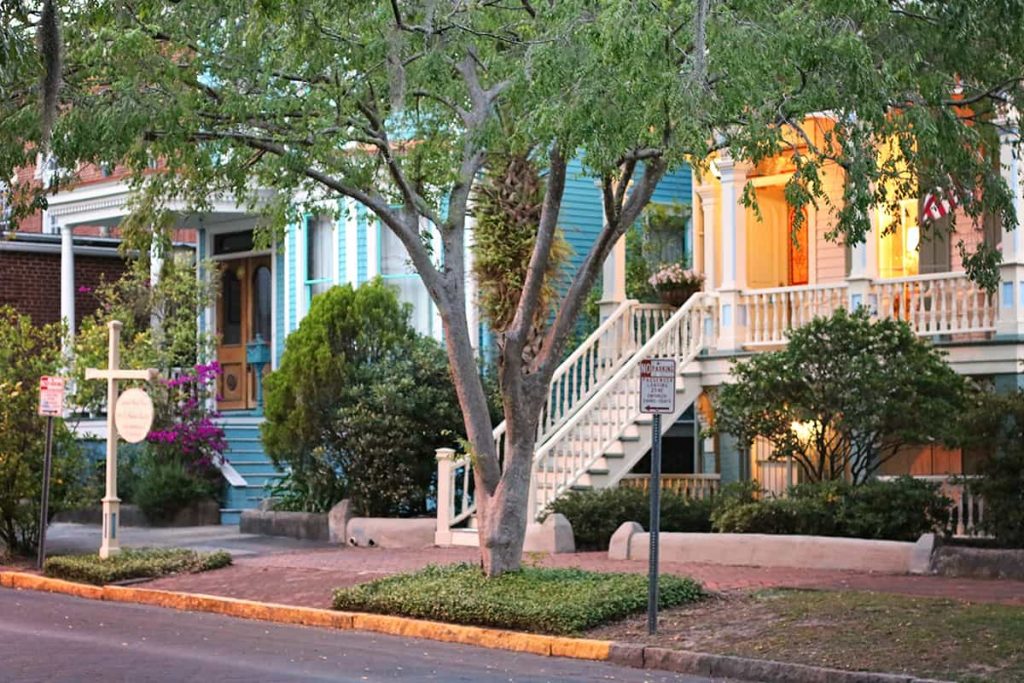 Street view looking towards two Victorian-style homes that are nicely landscaped and have flowers and American flags on the porch. A wooden sign reads Catherine Ward House Inn