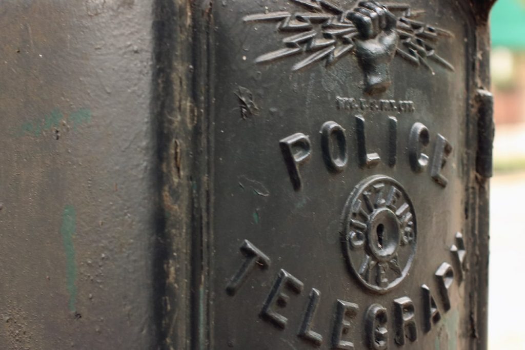Close-up of a black wrought-iron police telegraph box showing a fist holding lightning bolts and a key insert labeled Citizens Key