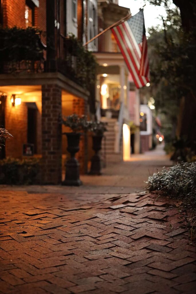 Low angle of a sidewalk on Jones Street in Savannah at dusk with low lighting and bricks that have been displaced causing safety issues