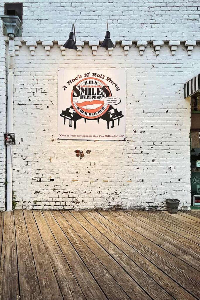 Whitewashed brick wall with a sign for Savannah Smiles Dueling Piano Bar