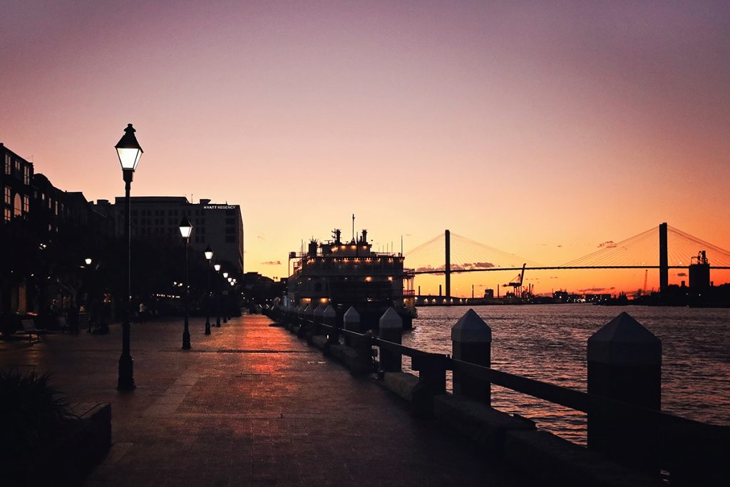 Riverfront plaza along River Street at dusk with the Savannah River and Talmadge bridge in the distance