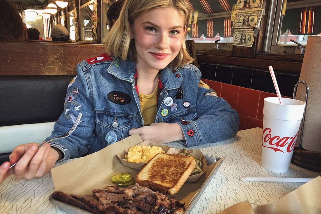 Blonde girl wearing a jean jacket sitting in front of a tray of the best BBQ in Savannah