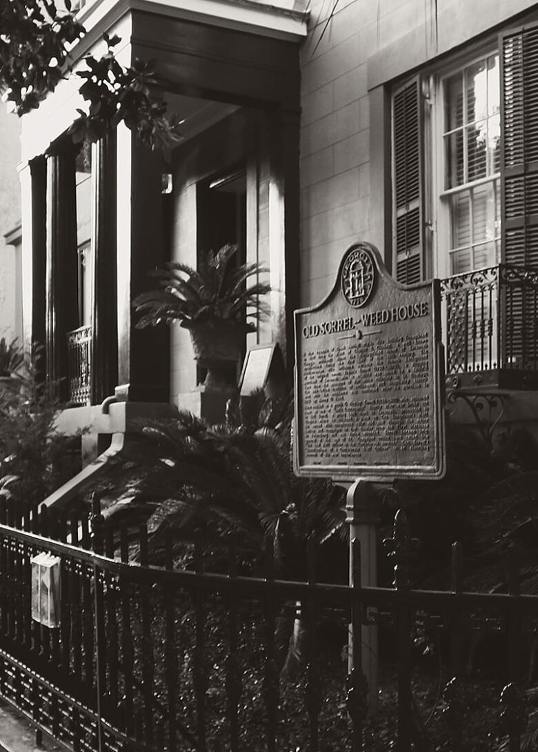 B&W side view of the front entrance to the Sorrel Weed House in Savannah, Georgia. The Historic Marker is visible in front of a curved wrought-iron fence