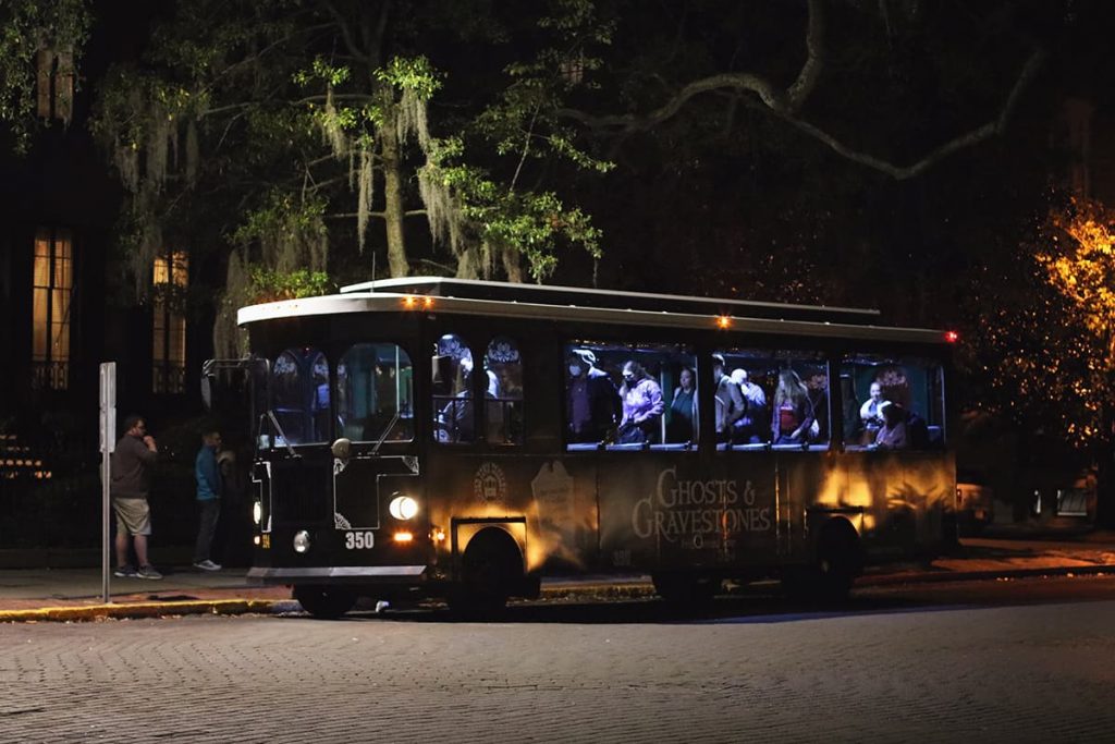 The Ghosts and Gravestones trolley at night parked beneath a large oak tree with Spanish moss hanging from its limbs