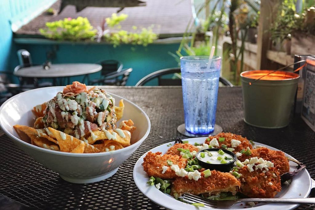 A plate of crispy fried green tomatoes sits next to a bowl of tuna tartare at an outdoor table at Driftaway Cafe