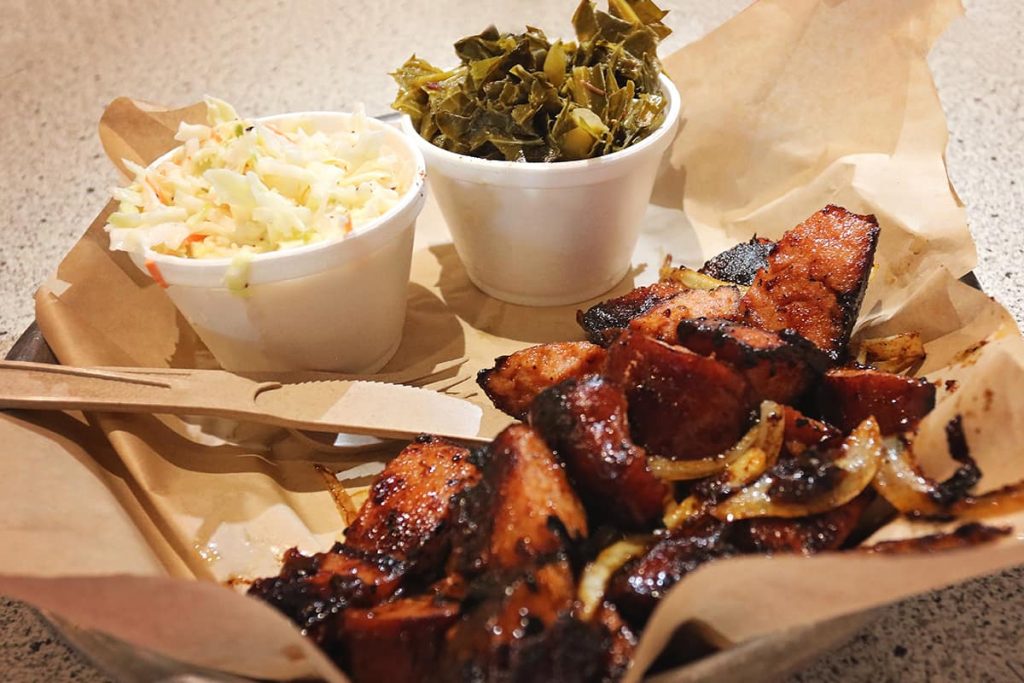 Sausage platter loaded with crispy brown sausage mixed with cooked onions. The two sides are cole slaw and collard greens