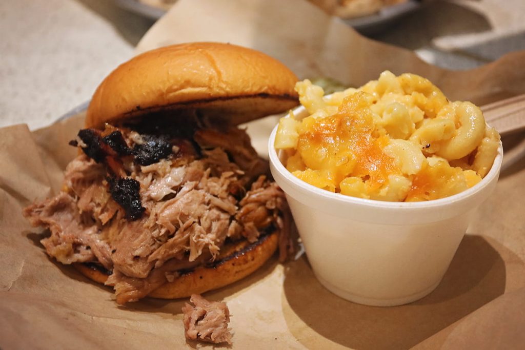 A pulled pork sandwich with a toasted bun and a side of perfectly cooked golden mac n' cheese